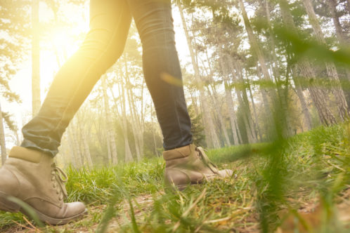 Female hiker wearing walking boots in sun dappled woods