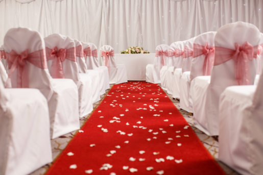 Red carpet with chairs arranged either side dressed with red ribbons, with flower petals scattered over leading to an altar for a civil wedding ceremony at mercure hotels