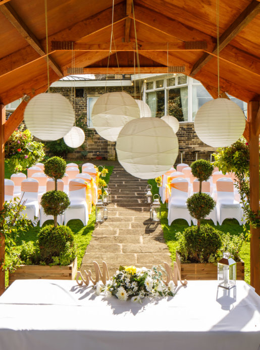 Close up shot of the wooden gazebo and hanging decorations of a wedding taking place in the luscious green garden at mercure bradford bankfield hotel