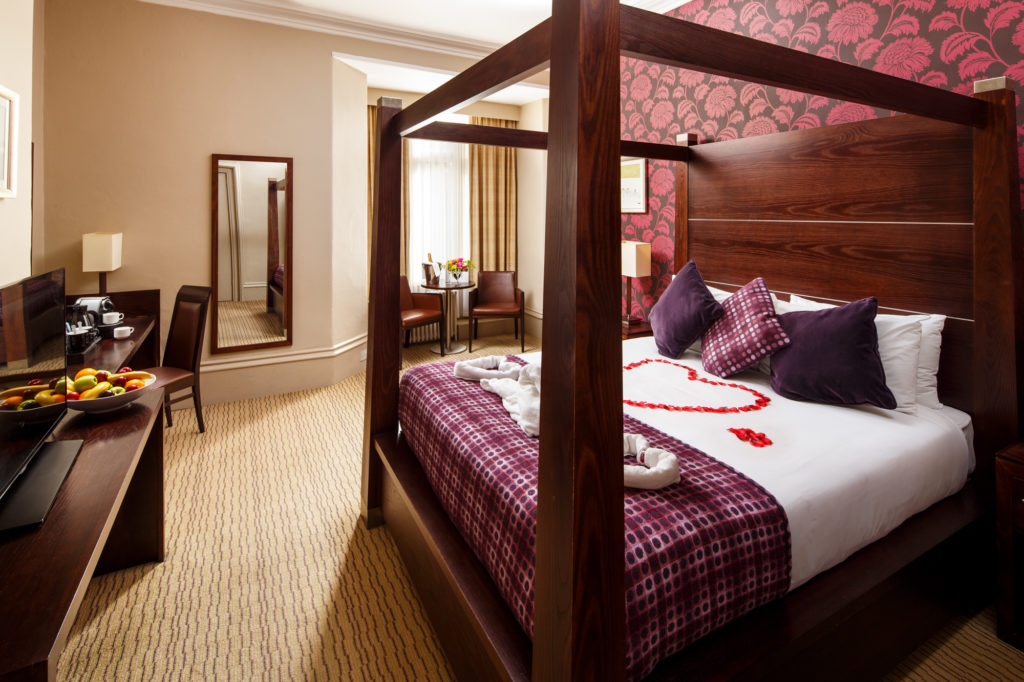 Privilege room with dark wood 4 poster bed with red rose petals formed on the bed for the happy couple