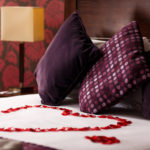 Close up shot of red rose petals shaped into a love heart on a four poster bed in a privilege room dressed as a bridal suite