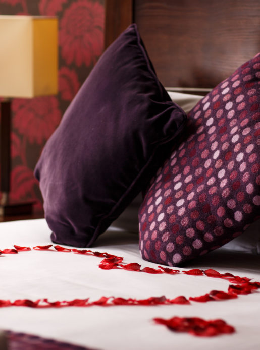 Close up shot of red rose petals shaped into a love heart on a four poster bed in a privilege room dressed as a bridal suite