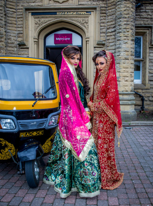 Two brides posing outside Mercure Bradford Bankfield Hotel in traditional Asian bridal dresses.
